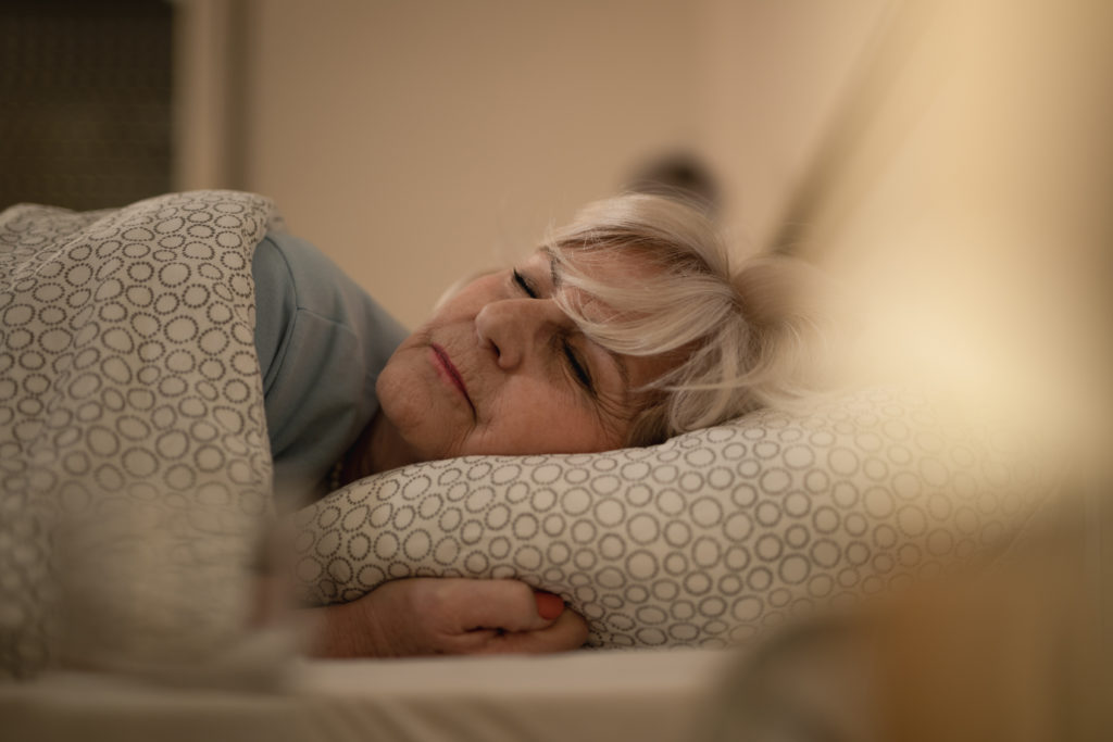 Senior woman sleeping on bed at night.